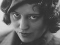 Nie wiem, kto jest na zdjęciu. Opis: Czarno-biała fotografia kobiety z kręconymi włosami i kapeluszem.