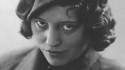 Nie wiem, kto jest na zdjęciu. Opis: Czarno-biała fotografia kobiety z kręconymi włosami i kapeluszem.