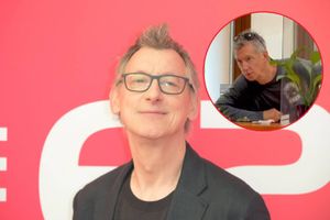 Mężczyzna w okularach, uśmiechnięty, w czarnym żakiecie na tle różowym. Na zdjęciu nie rozpoznałem polityka.
