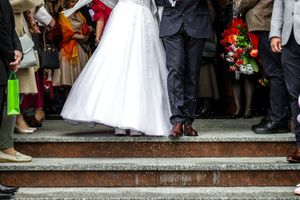 Para młoda schodzi ze schodów, wokół tłum gości, w powietrzu konfetti. Zieleniejsza torba w dłoni.