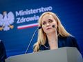 Na konferencji prasowej stoi kobieta w niebieskiej marynarce, mówi do mikrofonu.