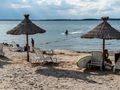 Plaża z parasolami, leżakami i w tle osoba na skuterze wodnym oraz spokojne wody jeziora.