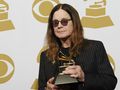 Mężczyzna w ciemnych okularach trzyma nagrodę Grammy na tle złotych symboli gramofonu.