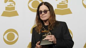 Mężczyzna w ciemnych okularach trzyma nagrodę Grammy na tle złotych symboli gramofonu.