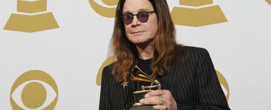 Mężczyzna w ciemnych okularach trzyma nagrodę Grammy na tle złotych symboli gramofonu.