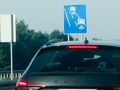 Zdjęcie przedstawia tył samochodu przed znakiem drogowym z kamerą monitorującą ruch.