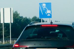 Zdjęcie przedstawia tył samochodu przed znakiem drogowym z kamerą monitorującą ruch.