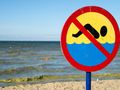 Znak zakazu pływania na tle morza i nieba. Plaża z falami w tle.