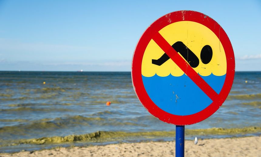 Znak zakazu pływania na tle morza i nieba. Plaża z falami w tle.