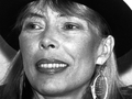 Joni Mitchell z szerokim uśmiechem, w kapeluszu, z dużymi kolczykami.