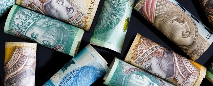 Zdjęcie zwiniętych banknotów w różnych nominałach, na tle ciemnej powierzchni.