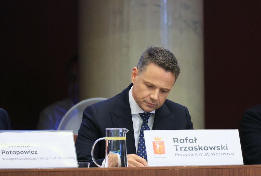 Na zdjęciu Rafał Trzaskowski, prezydent Warszawy, siedzący przy stole, piszący notatki.