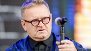 Mężczyzna w okularach trzyma mikrofon, w tle kolorowe światła. Niezidentyfikowany polityk.