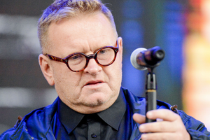 Mężczyzna w okularach trzyma mikrofon, w tle kolorowe światła. Niezidentyfikowany polityk.