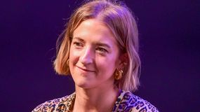 Lara Gessler z krótkimi blond włosami, w zwierzęcy wzór, uśmiechająca się na tle fioletowym.