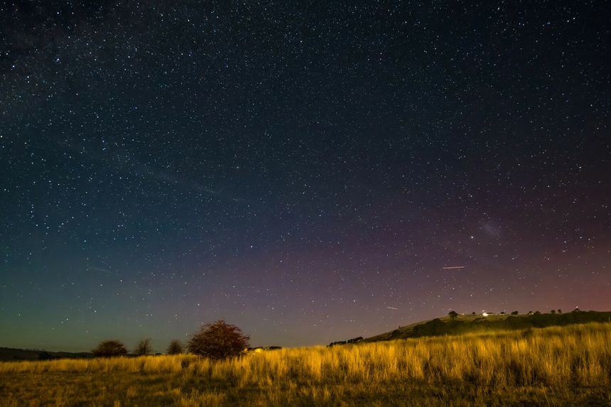 Widok nocnego nieba pełnego gwiazd nad łąką i wzniesieniem. Brak osób na zdjęciu.