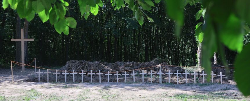Cmentarz z drewnianym krzyżem i białymi krzyżami wśród drzew. Miejsce pamięci.
