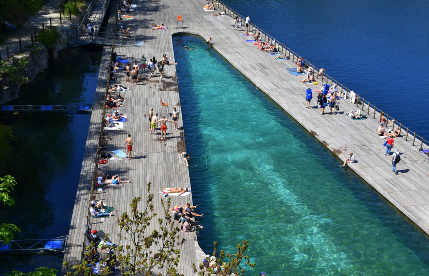Zdjęcie przedstawia letni wypoczynek nad wodą, plażowicze opalają się i pływają.