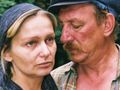 Na zdjęciu para, mężczyzna z wąsem blisko kobiety w chustce, w tle zieleń drzew.