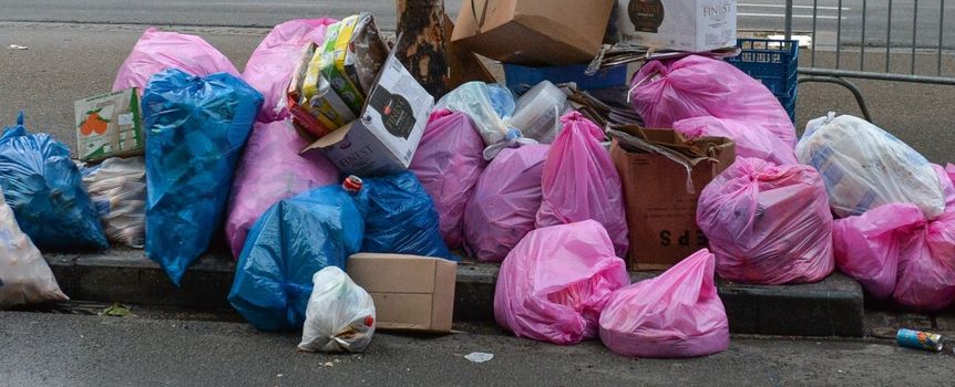 Zgrupowanie kolorowych worków na śmieci i kartonów na chodniku przy ulicy.