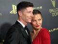 Na zdjęciu Robert Lewandowski z żoną, oboje w eleganckich strojach, pozują na czerwonym dywanie.