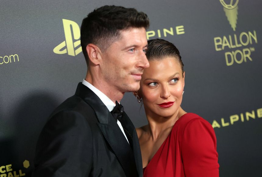 Na zdjęciu Robert Lewandowski z żoną, oboje w eleganckich strojach, pozują na czerwonym dywanie.