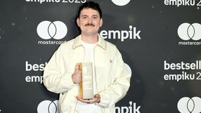 Mężczyzna w jasnej kurtce trzyma nagrodę na tle ciemnej ścianki z logo Empiku.