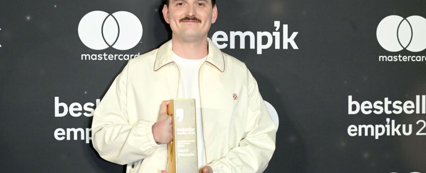 Mężczyzna w jasnej kurtce trzyma nagrodę na tle ciemnej ścianki z logo Empiku.