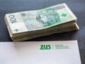 Stos rachunków banknotów 100 zł obok dokumentu ZUS.