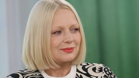 Kobieta z blond włosami i puchem na ramionach, uśmiechająca się na tle zielonej ścianki.