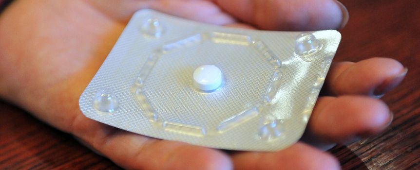 Na zdjęciu dłoń trzyma opakowanie tabletki, na które nałożona jest biały tablet.