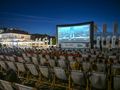 Kino plenerowe w nocy, widownia na leżakach, wyświetlany film na dużym ekranie.