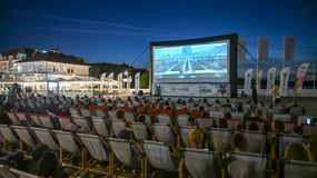 Kino plenerowe w nocy, widownia na leżakach, wyświetlany film na dużym ekranie.