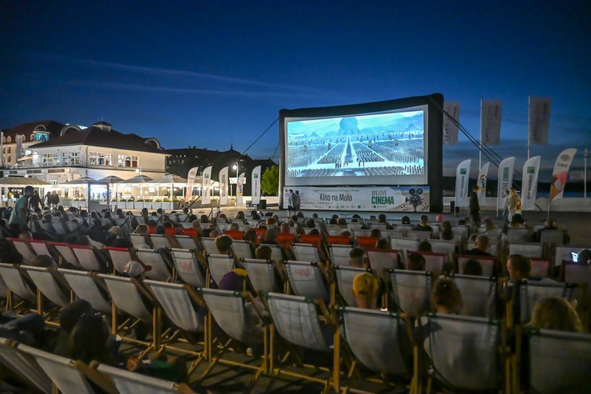 Kino plenerowe w nocy, widownia na leżakach, wyświetlany film na dużym ekranie.