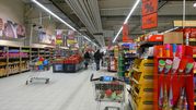 Wnętrze supermarketu z zakupami w koszykach, reklamami i półkami z produktami.