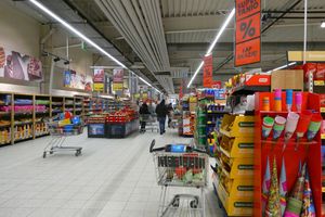 Wnętrze supermarketu z zakupami w koszykach, reklamami i półkami z produktami.