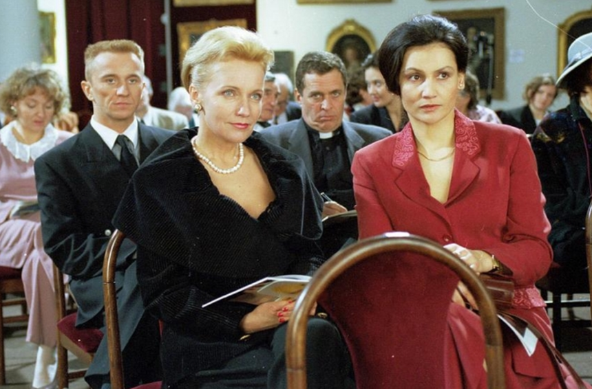 Na zdjęciu dwie elegancko ubrane kobiety siedzą na widowni. W tle inni uczestnicy wydarzenia.