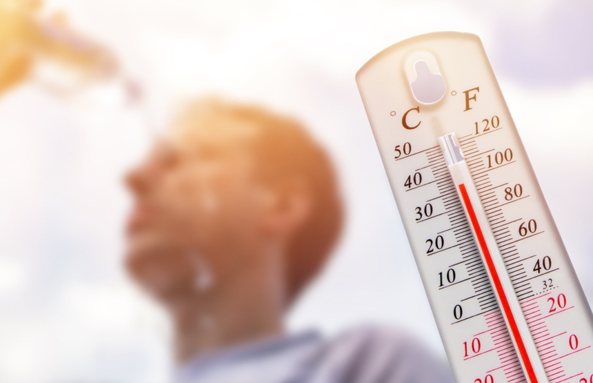 Mężczyzna z mokrym czołem patrzy w górę, w tle termometr wskazujący wysoką temperaturę.