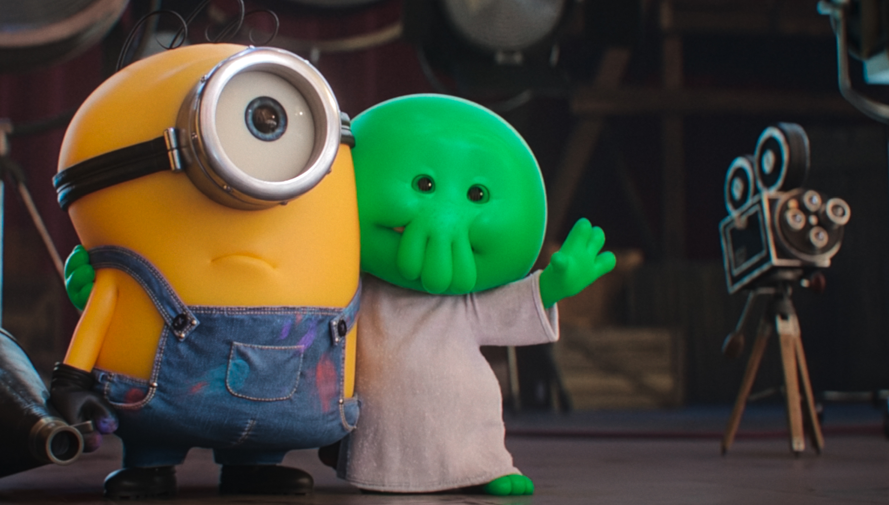 Na zdjęciu dwa kolorowe stworki: żółty minion i zielony potwór w białej szacie na planie filmowym.