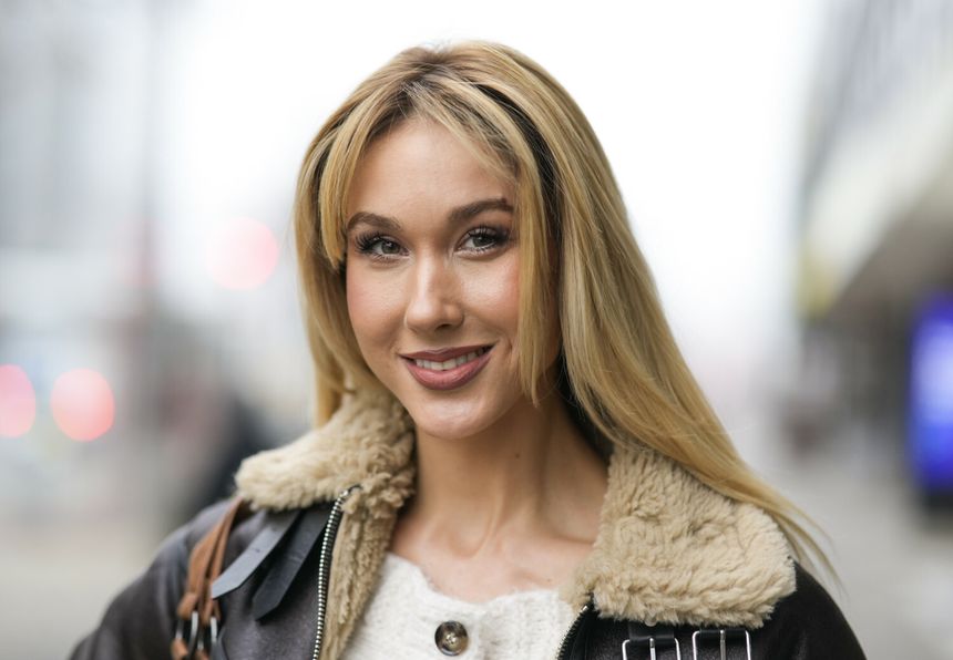 Ida Nowakowska z długimi, blond włosami, uśmiecha się w miejskim otoczeniu, w ciepłej kurtce.