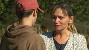 Kobieta w bluzie z dekoltem rozmawia z młodym mężczyzną, wygląda na wzruszoną.