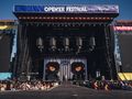 Opis ALT: Scena festiwalowa z wielkimi ekranami, tłum publiczności czeka na występ artysty.