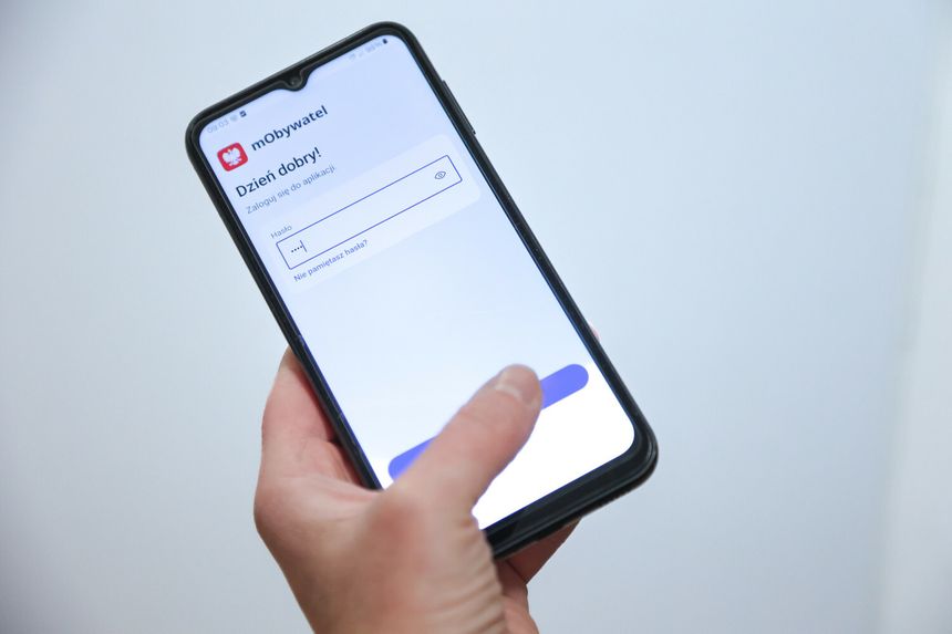 Na zdjęciu widoczny jest telefon komórkowy z ekranem aplikacji mObywatel. Widać ekran logowania.