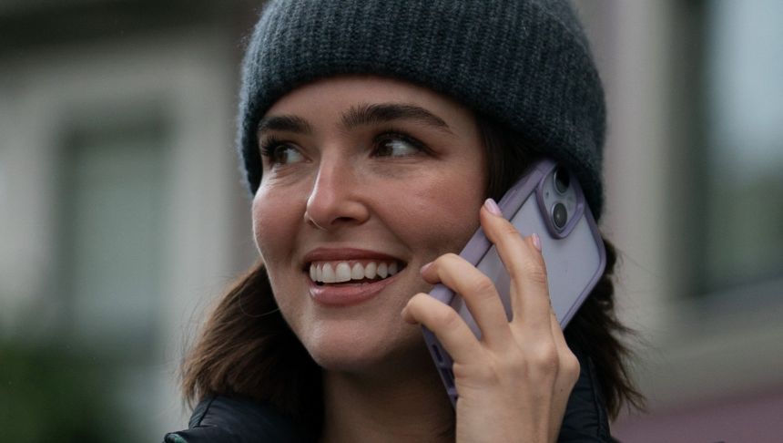 Kobieta w czapce rozmawia przez telefon, uśmiechając się i wyglądając na zadowoloną.