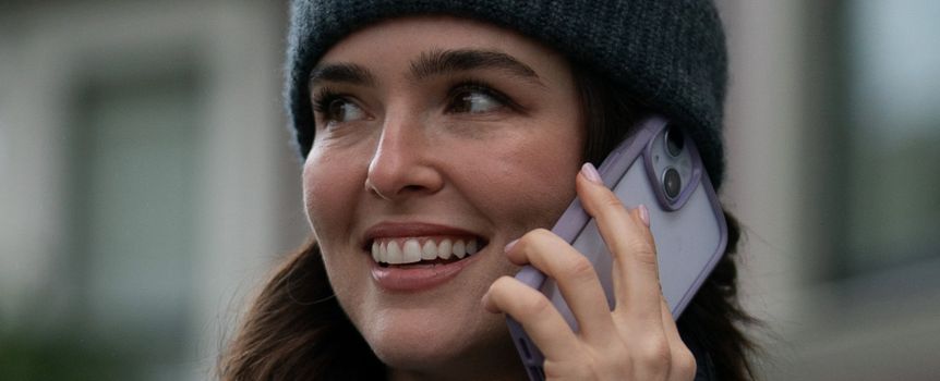 Kobieta w czapce rozmawia przez telefon, uśmiechając się i wyglądając na zadowoloną.
