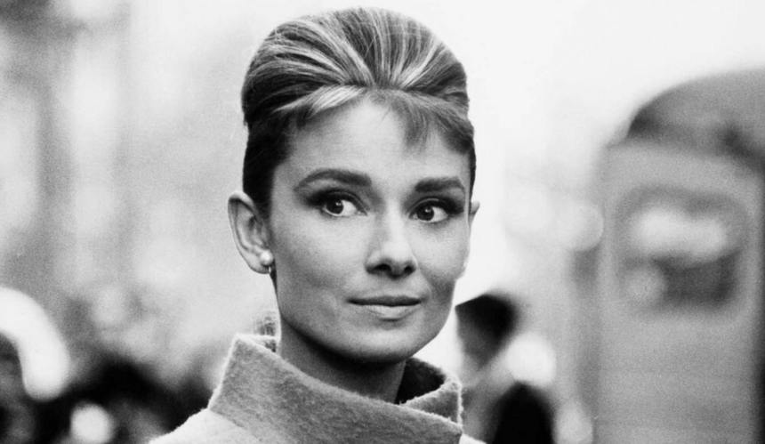 Czarno-białe zdjęcie Audrey Hepburn w płaszczu i koku