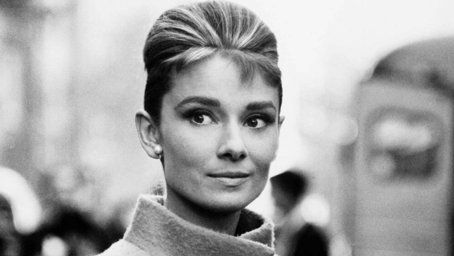 Czarno-białe zdjęcie Audrey Hepburn w płaszczu i koku