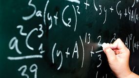 Na czarnej tablicy widoczne ręczne pisanie równań matematycznych białą kredą.