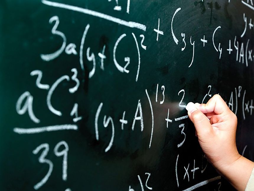Na czarnej tablicy widoczne ręczne pisanie równań matematycznych białą kredą.
