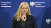 Kobieta z długimi, blond włosami, przemawiająca na konferencji z logo Ministerstwa Zdrowia.